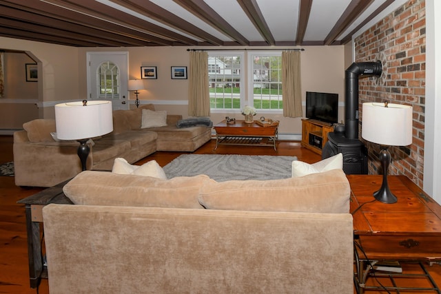 living area featuring arched walkways, a wood stove, beam ceiling, and wood finished floors