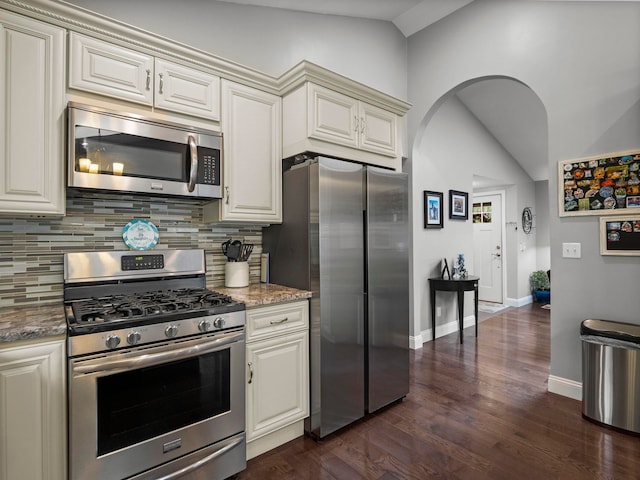 kitchen with light stone countertops, stainless steel appliances, lofted ceiling, and backsplash