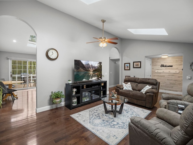 living area featuring baseboards, lofted ceiling with skylight, ceiling fan, arched walkways, and dark wood-style floors