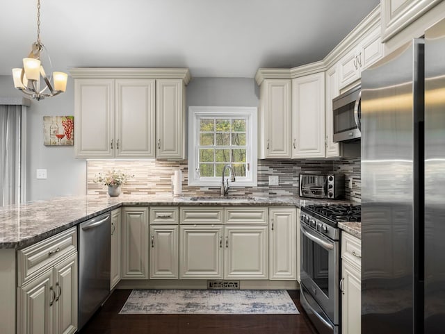 kitchen featuring a peninsula, decorative backsplash, a sink, appliances with stainless steel finishes, and a chandelier