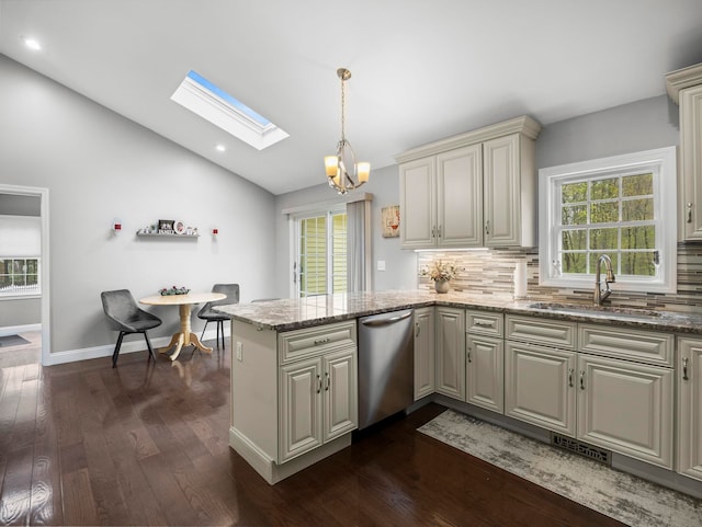 kitchen with a sink, a peninsula, vaulted ceiling with skylight, dishwasher, and cream cabinetry