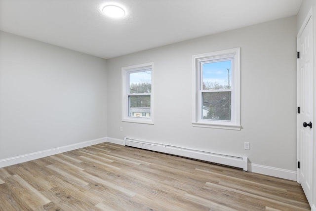 spare room featuring a baseboard radiator, baseboards, and light wood finished floors