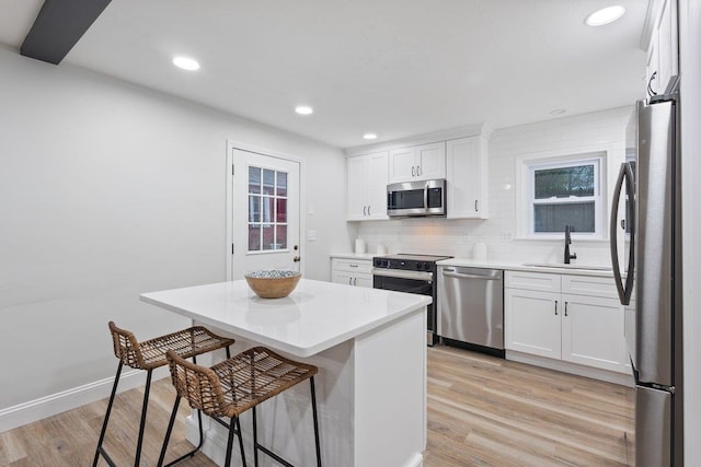 kitchen featuring light wood-type flooring, appliances with stainless steel finishes, a sink, and a kitchen bar