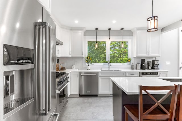 kitchen featuring pendant lighting, premium appliances, white cabinetry, backsplash, and light countertops