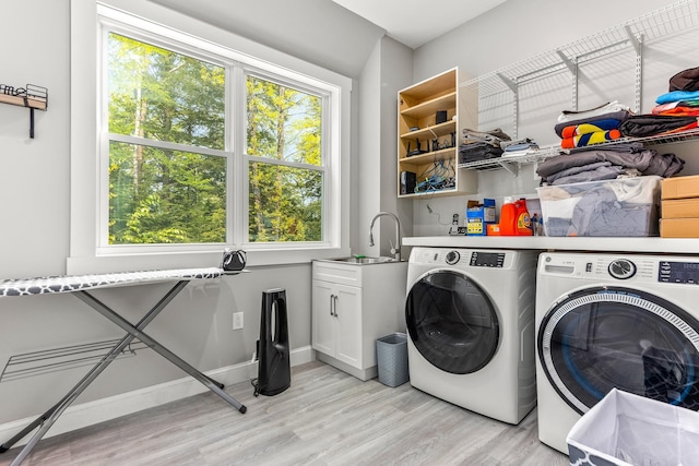laundry area with a sink, cabinet space, washing machine and clothes dryer, light wood finished floors, and a wealth of natural light