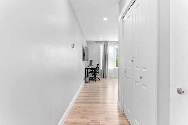 hallway featuring baseboards, light wood finished floors, and recessed lighting