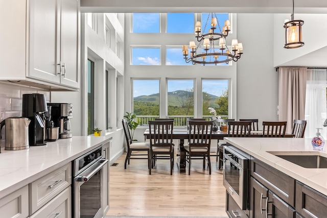 kitchen with a notable chandelier, light stone counters, stainless steel oven, hanging light fixtures, and light wood-style floors
