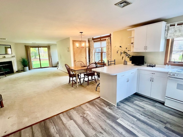 kitchen with a peninsula, wood finished floors, visible vents, light countertops, and white range with electric stovetop