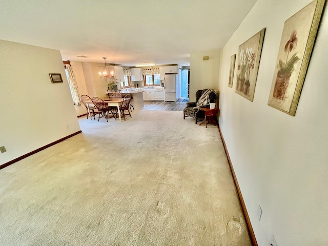 interior space with light colored carpet, a chandelier, and baseboards