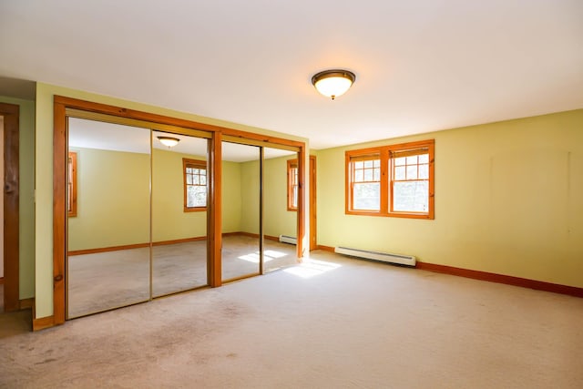 unfurnished bedroom with a baseboard heating unit, carpet flooring, two closets, and baseboards