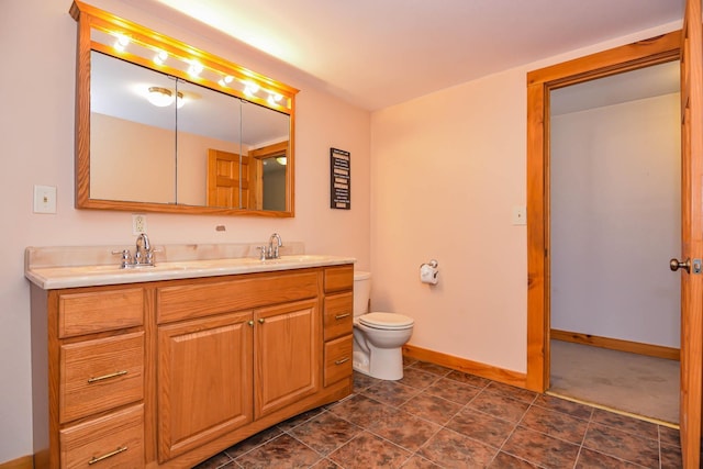 bathroom featuring double vanity, toilet, baseboards, and a sink