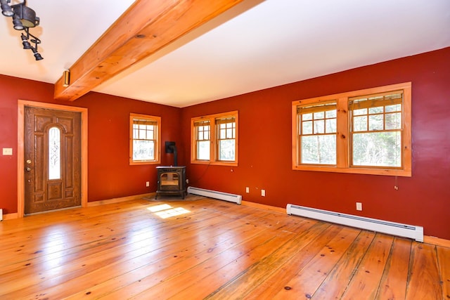 entryway with a wood stove, beamed ceiling, light wood finished floors, and a baseboard heating unit