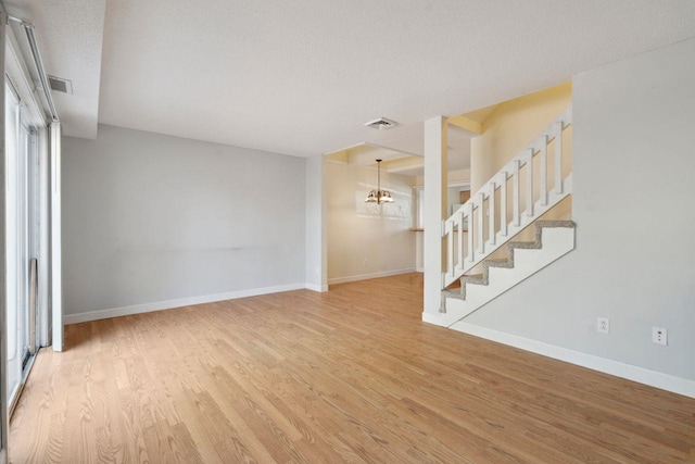 unfurnished living room with stairway, an inviting chandelier, baseboards, and wood finished floors