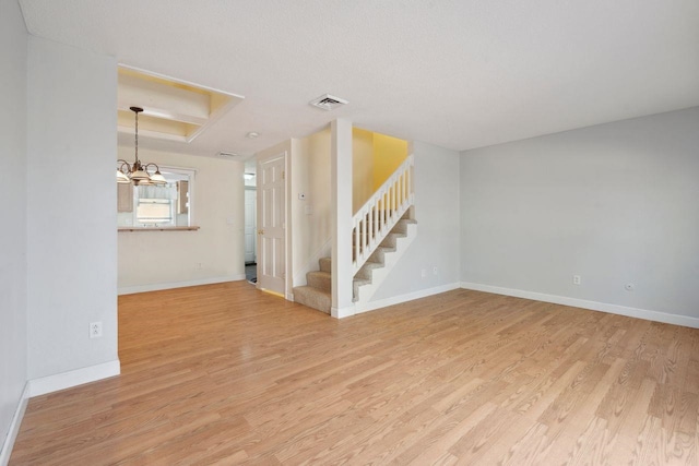 unfurnished living room with stairs, light wood-type flooring, visible vents, a chandelier, and baseboards