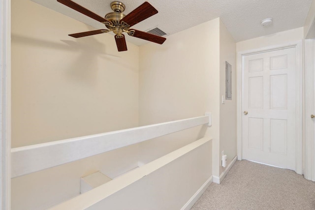 corridor with electric panel, a textured ceiling, visible vents, baseboards, and light colored carpet