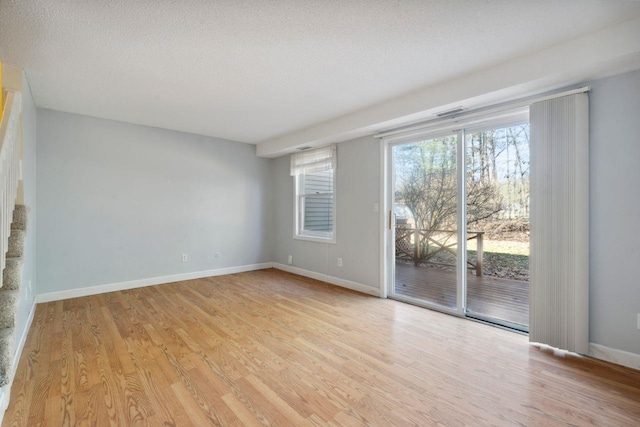 empty room with baseboards, light wood finished floors, and a textured ceiling