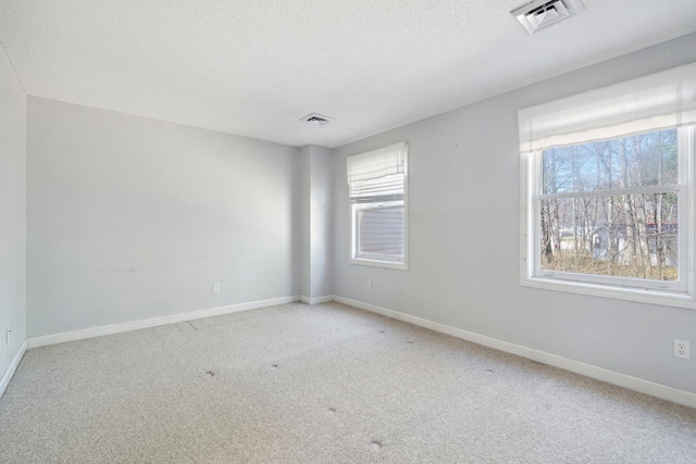 carpeted empty room featuring a textured ceiling, baseboards, and visible vents