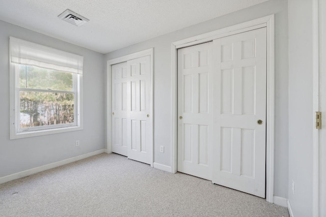unfurnished bedroom with a textured ceiling, baseboards, visible vents, multiple closets, and carpet floors