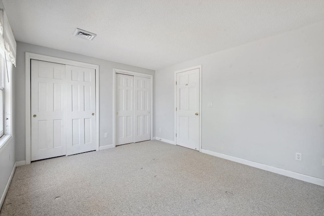 unfurnished bedroom featuring a textured ceiling, baseboards, carpet flooring, visible vents, and multiple closets
