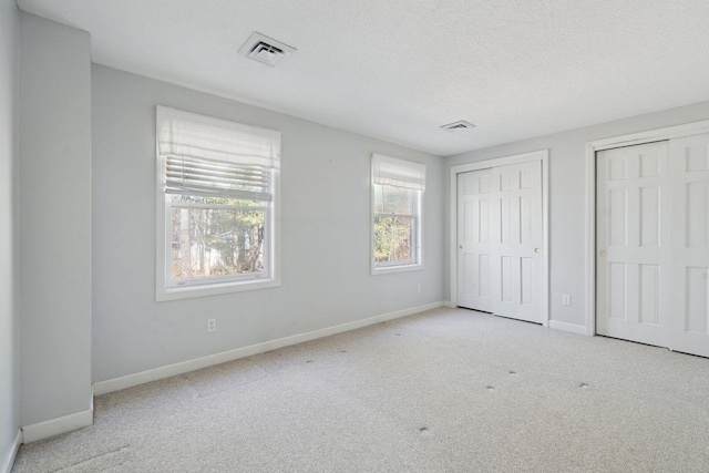 unfurnished bedroom featuring multiple windows, two closets, and carpet floors