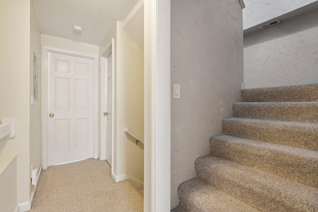 staircase with baseboards, visible vents, carpet, and a textured wall