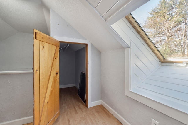additional living space featuring lofted ceiling, a textured wall, baseboards, and light wood-type flooring