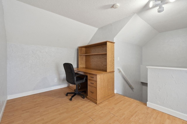 office with lofted ceiling, a textured ceiling, a textured wall, baseboards, and light wood-style floors