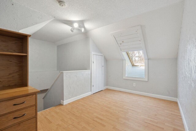 additional living space with a textured ceiling, baseboards, vaulted ceiling, light wood-style floors, and a textured wall