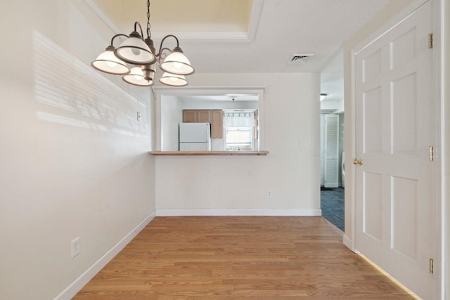 unfurnished dining area featuring an inviting chandelier, baseboards, visible vents, and light wood-style floors