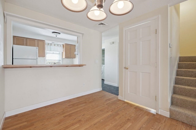 unfurnished living room featuring light wood-style flooring, baseboards, visible vents, stairs, and a chandelier