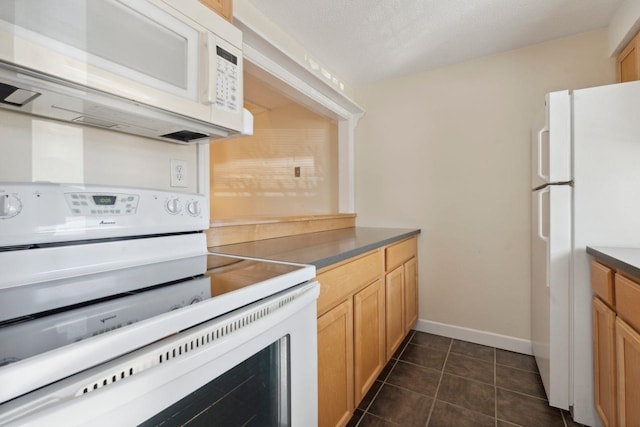 kitchen with baseboards, white appliances, dark countertops, and dark tile patterned floors