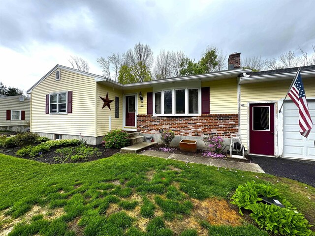 ranch-style home with brick siding, a garage, a chimney, and a front yard