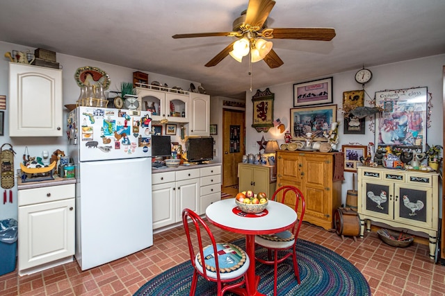 kitchen with freestanding refrigerator, brick patterned floor, a ceiling fan, and white cabinets