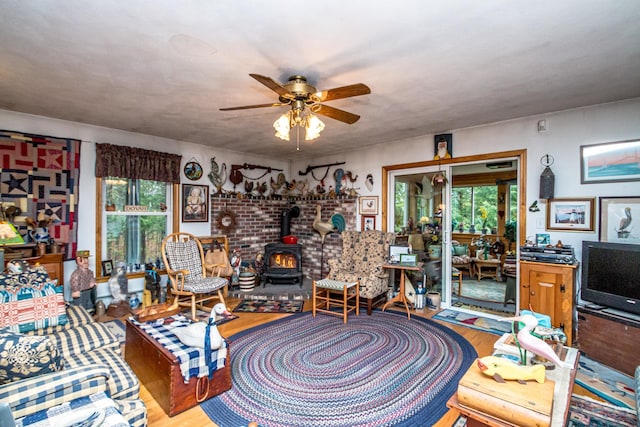 living area featuring a wood stove, a wealth of natural light, ceiling fan, and wood finished floors