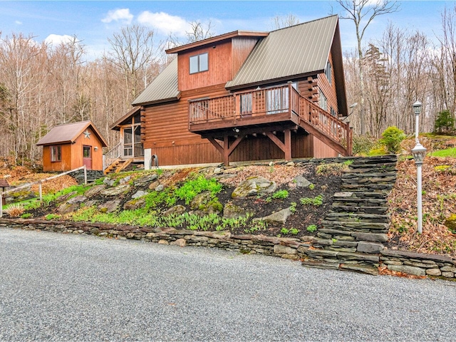exterior space with log siding, an outdoor structure, a deck, stairway, and metal roof
