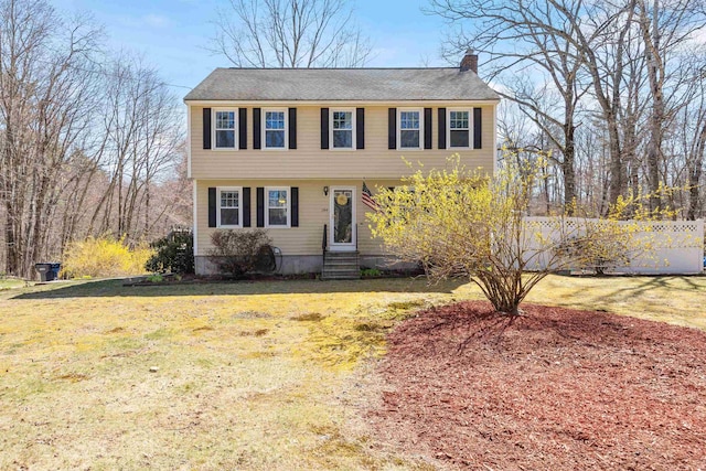 colonial inspired home with a chimney, entry steps, a front yard, and fence