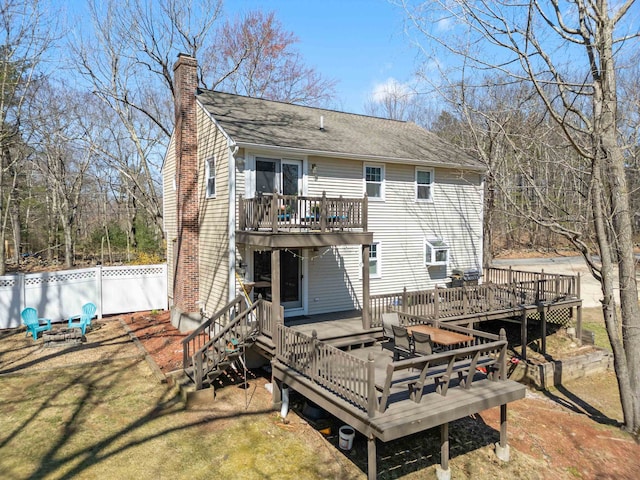 rear view of property featuring a chimney, a yard, fence, a shingled roof, and a wooden deck
