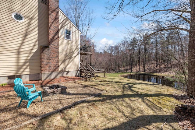 view of yard featuring stairs, a fire pit, and a deck with water view