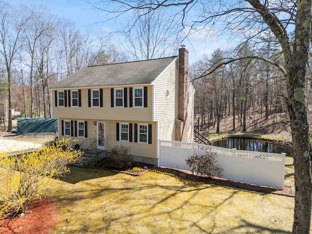 colonial house featuring a chimney, a water view, and fence