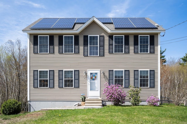 colonial-style house with entry steps, roof mounted solar panels, and a front yard