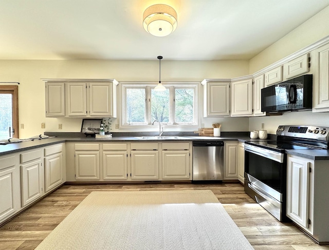 kitchen with stainless steel appliances, a sink, dark countertops, hanging light fixtures, and light wood-type flooring