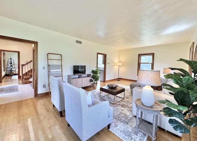 living room featuring stairway, light wood-style flooring, and baseboards