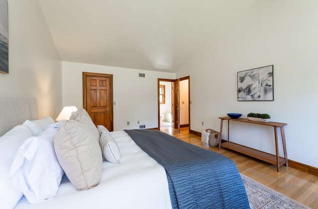 bedroom with light wood-style floors, vaulted ceiling, and baseboards