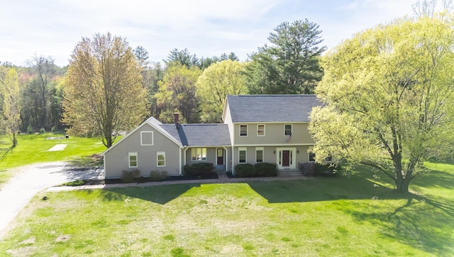 colonial-style house featuring a front lawn, a chimney, and roof with shingles
