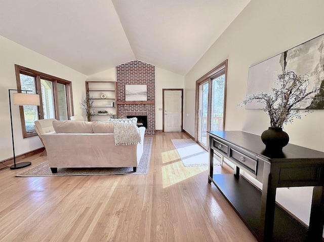 living room with vaulted ceiling, light wood finished floors, a brick fireplace, and baseboards