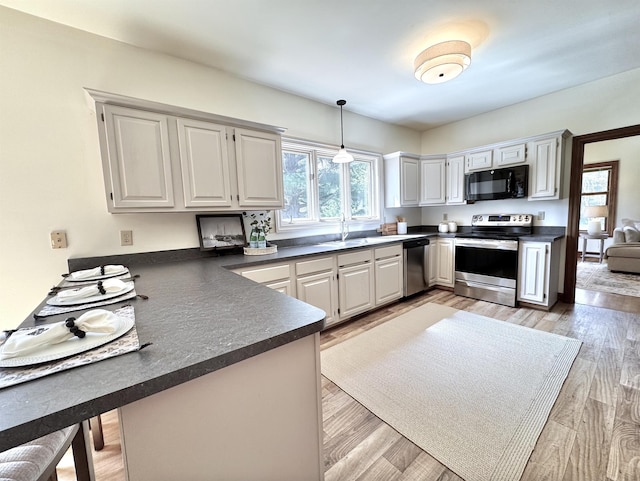 kitchen with stainless steel appliances, dark countertops, a peninsula, a sink, and plenty of natural light
