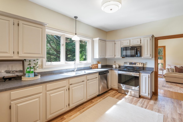 kitchen with appliances with stainless steel finishes, a sink, dark countertops, decorative light fixtures, and light wood-style floors