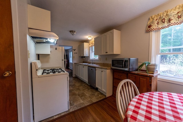 kitchen featuring under cabinet range hood, white gas range, stainless steel microwave, a sink, and dishwashing machine