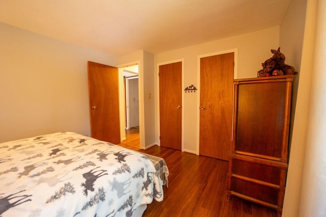 bedroom featuring dark wood-style floors, two closets, and baseboards