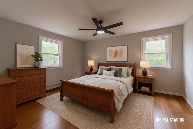 bedroom with a baseboard heating unit, multiple windows, wood finished floors, and baseboards